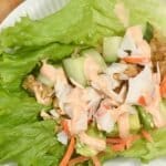 Lettuce wrap with crap, cucumber, avocado and carrots in a plate topped with spicy mayo