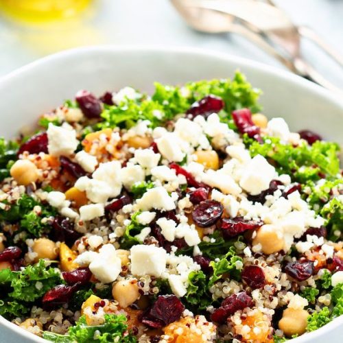 A salad bowl with quinoa, kale, chickpeas, cranberries, roasted squash, topped with crumbled cheese.