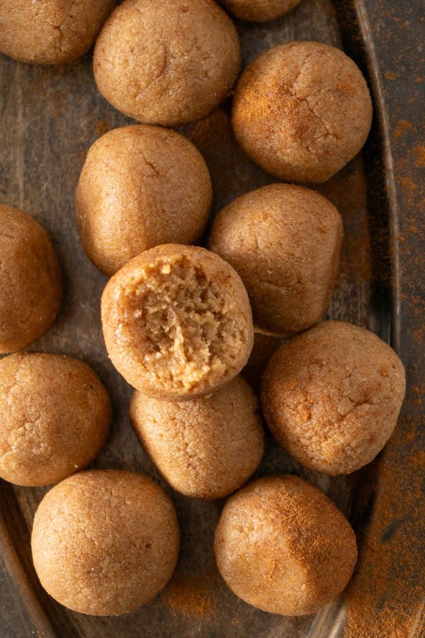 A close-up of several round, brown Churro Protein Balls on a tray, with one ball showing a bite taken out.