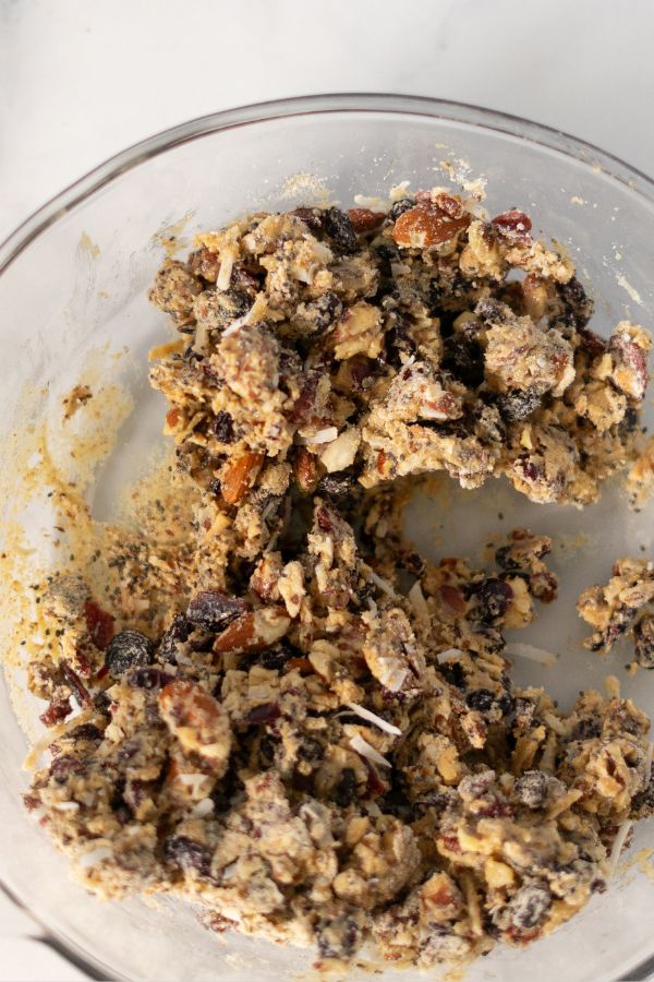 A glass bowl containing a thick mixture of dried fruits and nuts, similar to the wholesome blends found in Kind Bars, is partially combined with dough and sits on a white surface.