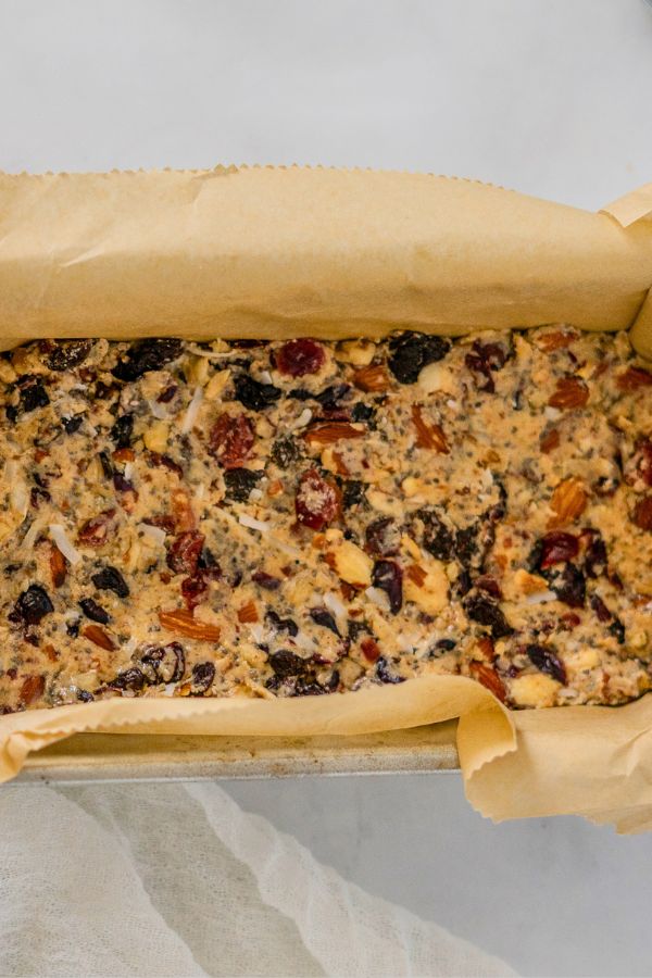 A loaf pan lined with parchment paper filled with unbaked fruit and nut cake batter, reminiscent of the wholesome ingredients found in Kind Bars, viewed from above.