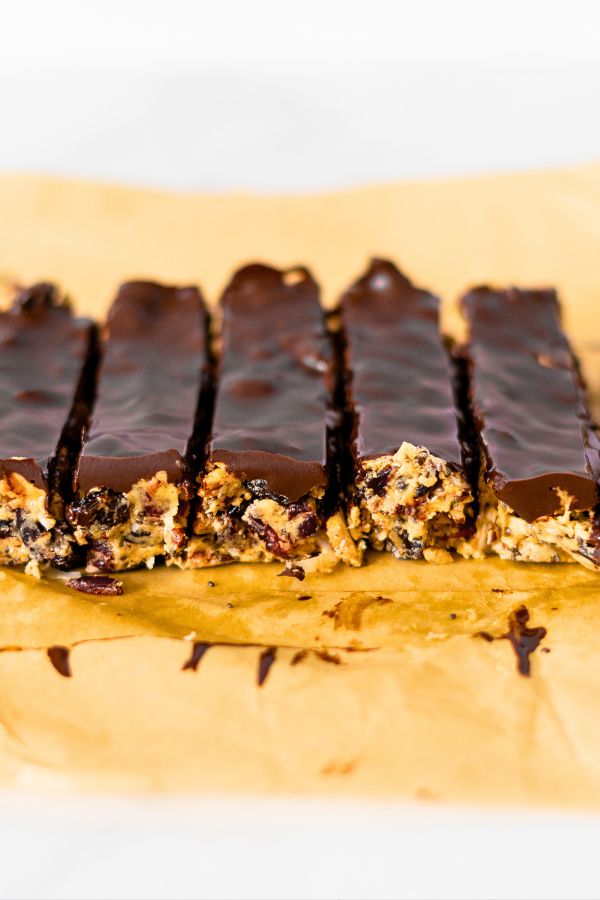 Five Kind Bars, chocolate-covered granola bars, are arranged in a row on brown parchment paper, with one bar partially eaten.
