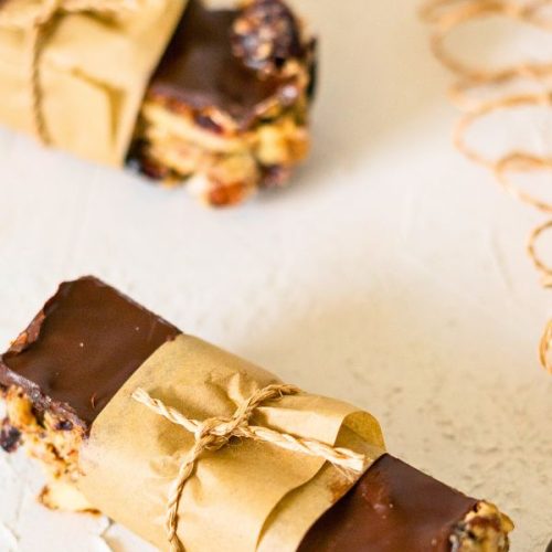 Two chocolate-topped Kind Bars wrapped in brown paper and tied with string are placed on a light-colored surface.
