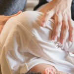 A person in a white shirt lies on their side while another person uses their hands to adjust or massage their shoulder and back, demonstrating the techniques often used in chiropractic care.