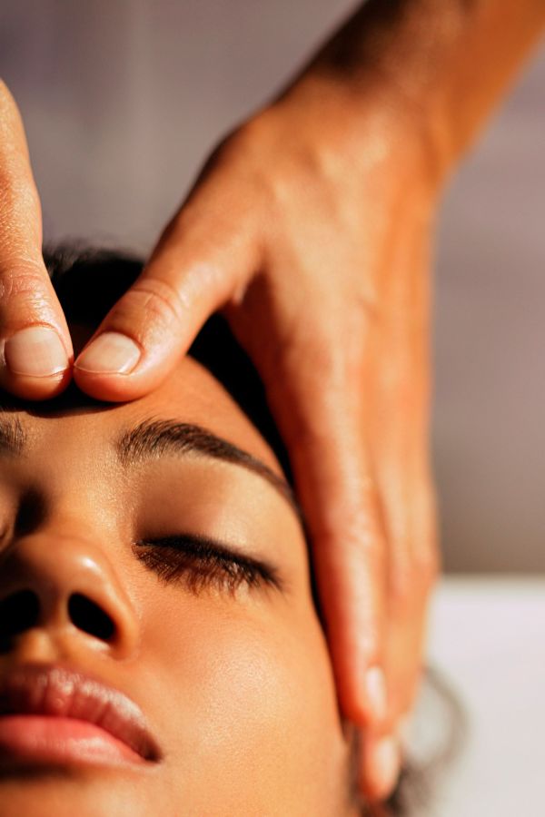 Close-up of a person receiving a forehead massage with two hands gently pressing on their forehead while their eyes are closed, offering a calming massage for stress and anxiety.
