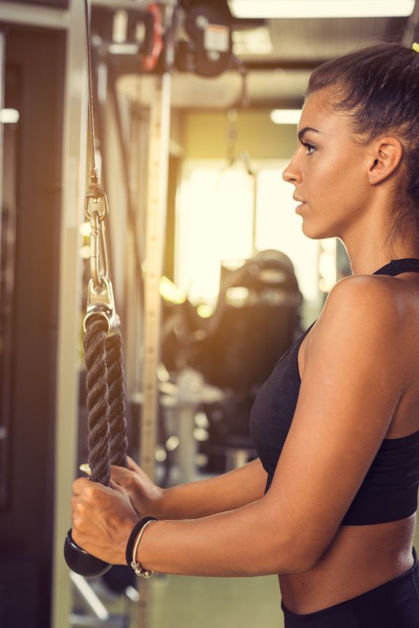A woman in athletic wear performs a rope tricep pushdown exercise at a gym, holding the rope attachment of a cable machine for effective tricep extensions.